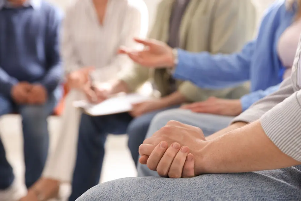 rehab-insurance-mental-health-services Person clasps hands together during group discussion of insurance coverage for rehab.